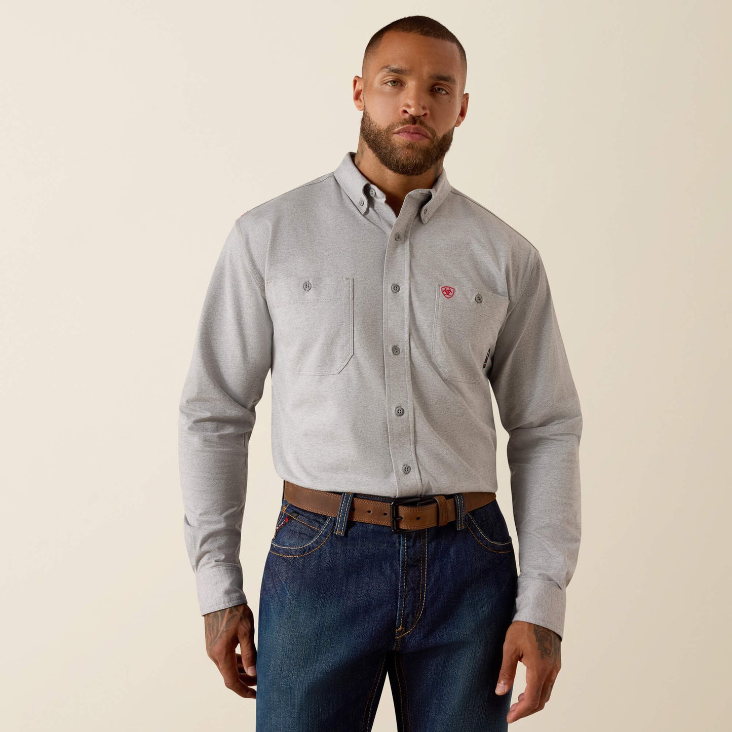 Man wearing a gray button-up shirt and blue jeans on a beige background