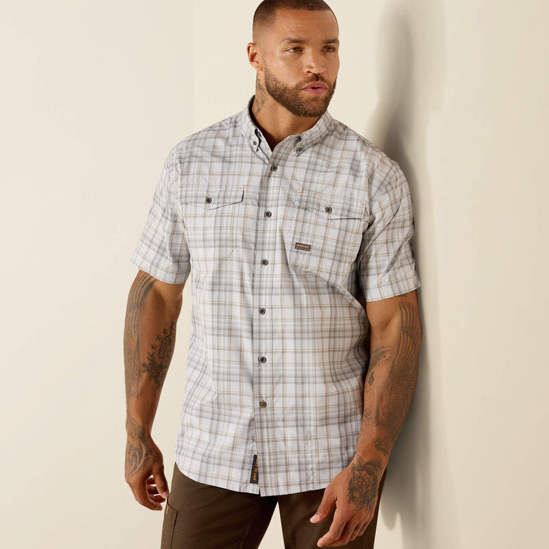 Man wearing a plaid shirt leaning against a beige wall