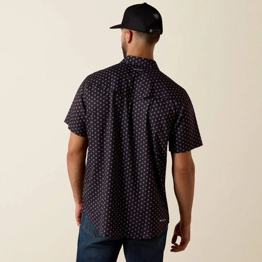 Man wearing a dark patterned shirt and black cap on a beige background