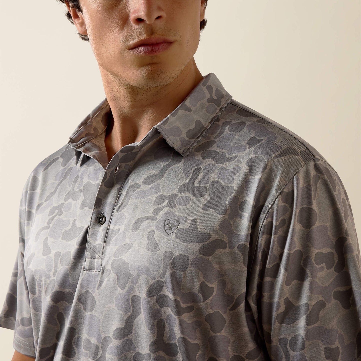 Man wearing a camouflage-patterned polo shirt against a neutral background
