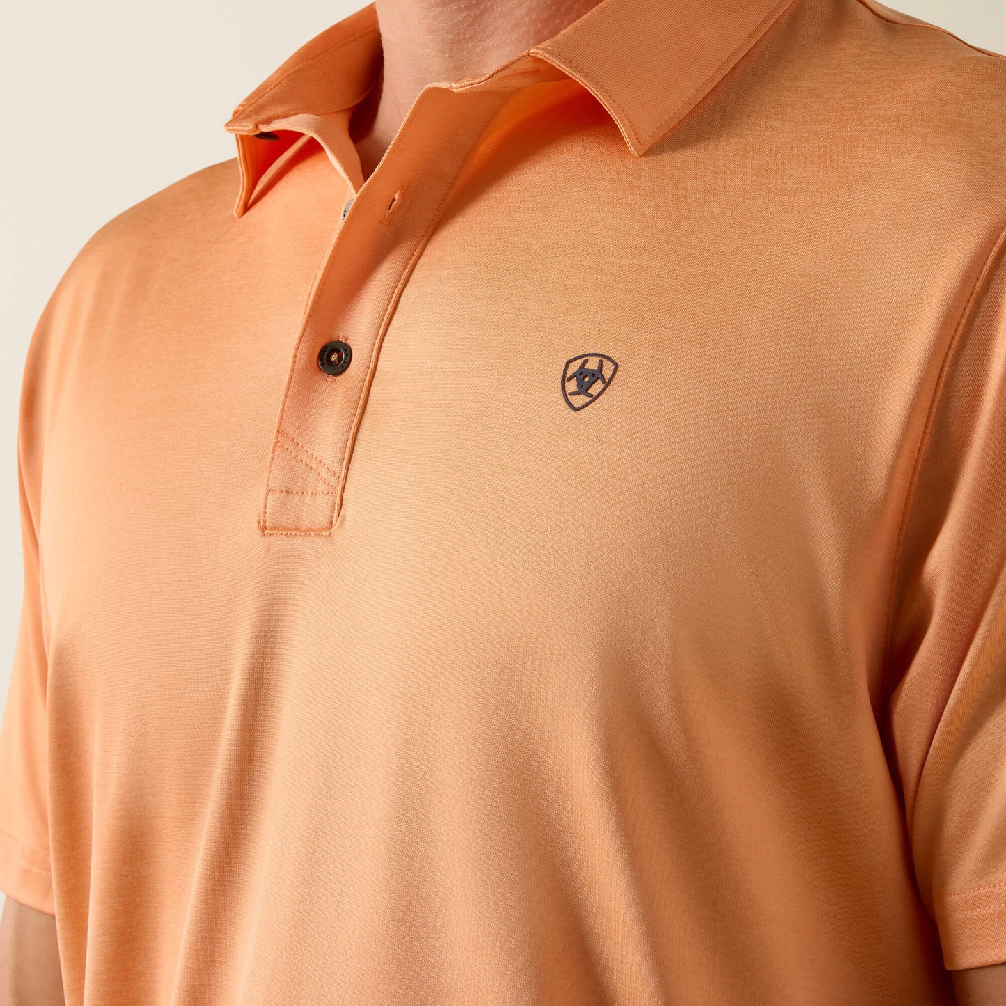 Close-up of an orange polo shirt with a brand logo on a light gray background
