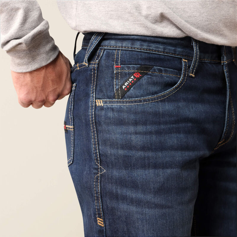 Close-up of a person wearing dark blue denim jeans, showing the back pocket with a visible Apatite brand tag and a hand pulling the waistband.