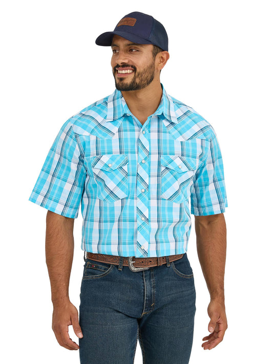Man in turquoise plaid short sleeve western shirt, jeans, and navy trucker hat