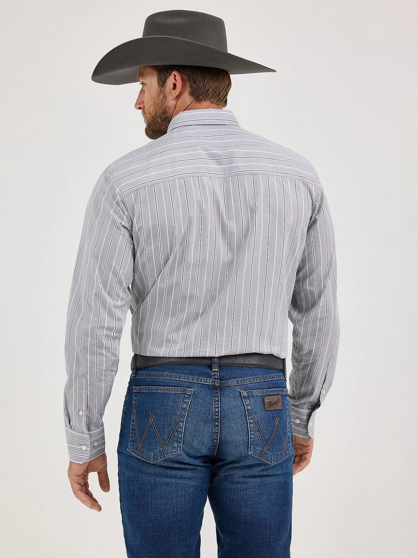 Man in a gray striped western shirt, blue jeans, and cowboy hat shown from the back