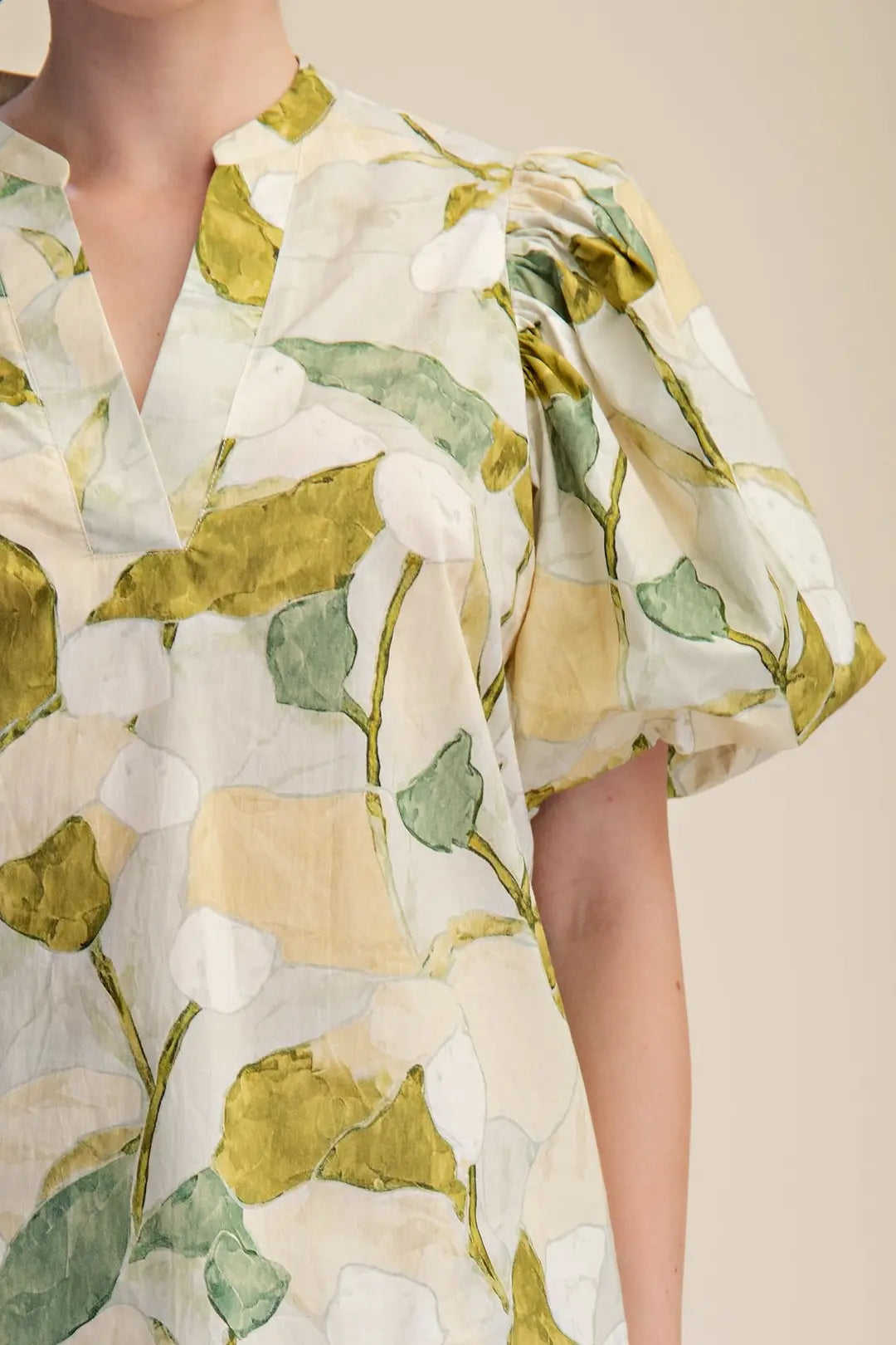 Close-up of a person wearing a white dress with green leaf patterns on a beige background