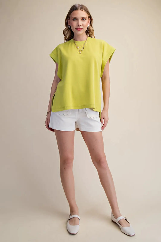 Woman wearing a bright yellow top and white shorts on a beige background