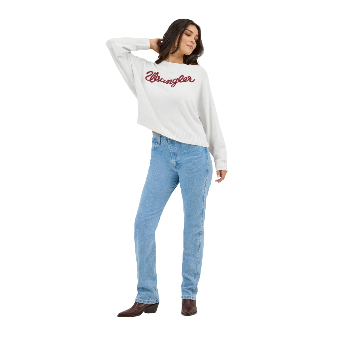 Woman wearing a white Wrangler sweater, blue high-waisted jeans, and brown boots