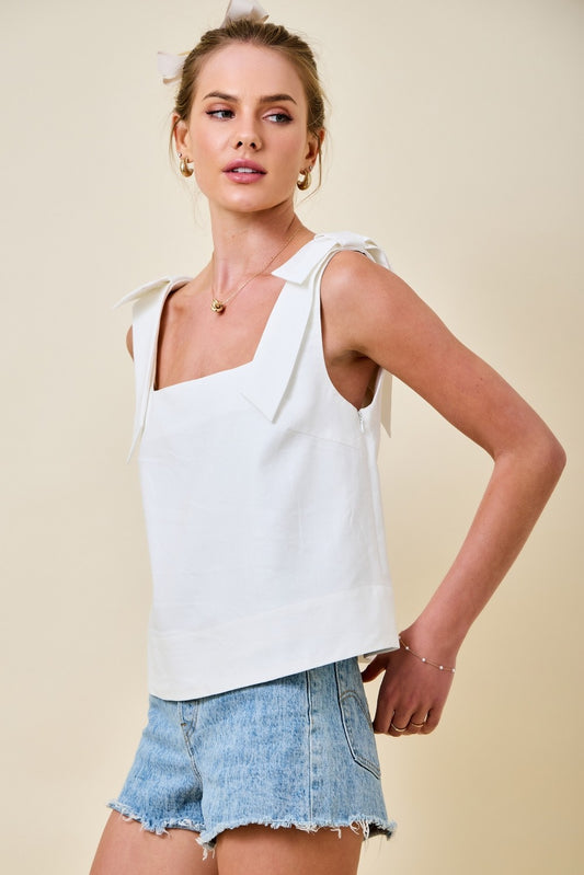 Woman wearing a white sleeveless top and denim shorts on a beige background
