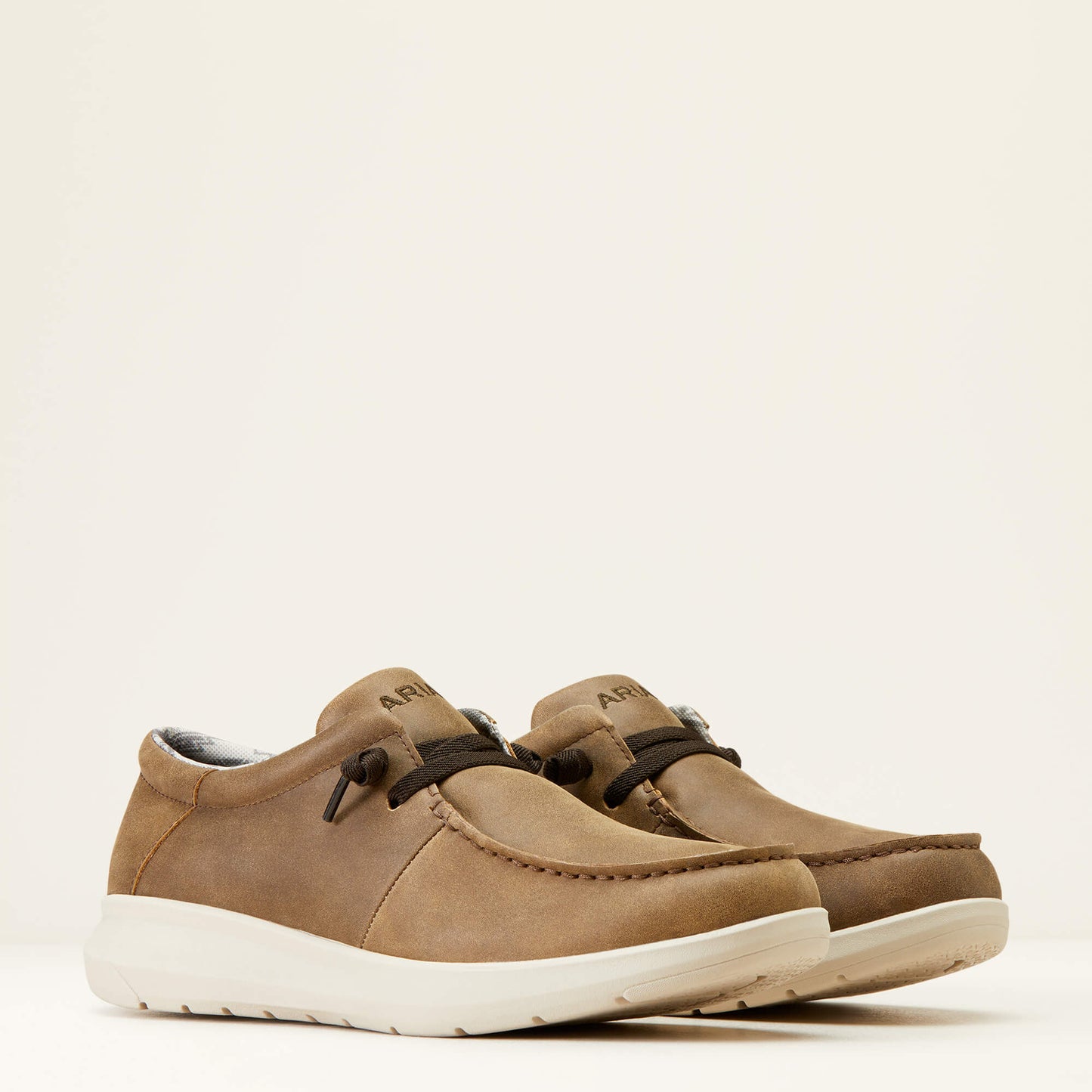 Brown suede casual slip-on shoes with white rubber soles and black laces on a plain background.