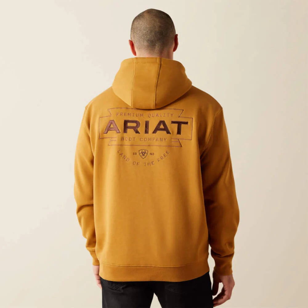 Man wearing mustard yellow hoodie with large 'ARIAT' logo on back, casual clothing style