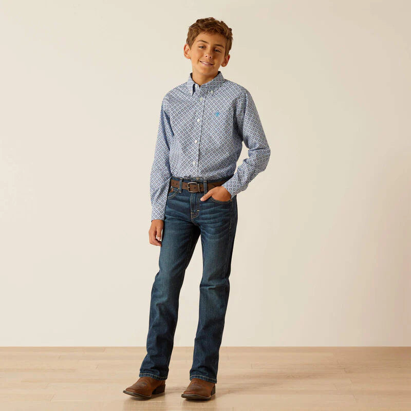 Boy wearing patterned blue button-up shirt, blue jeans, brown belt, and boots indoors