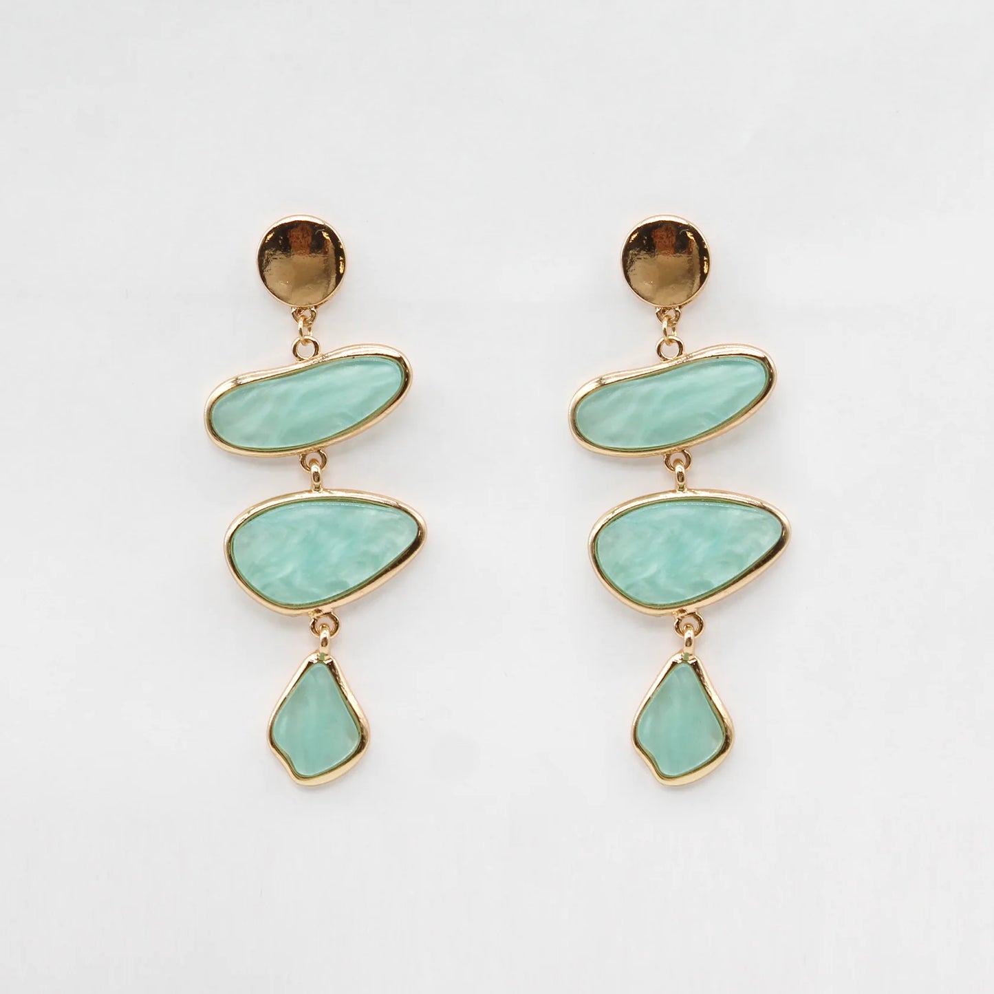 Pair of earrings with gold accents and turquoise stones on a light gray background