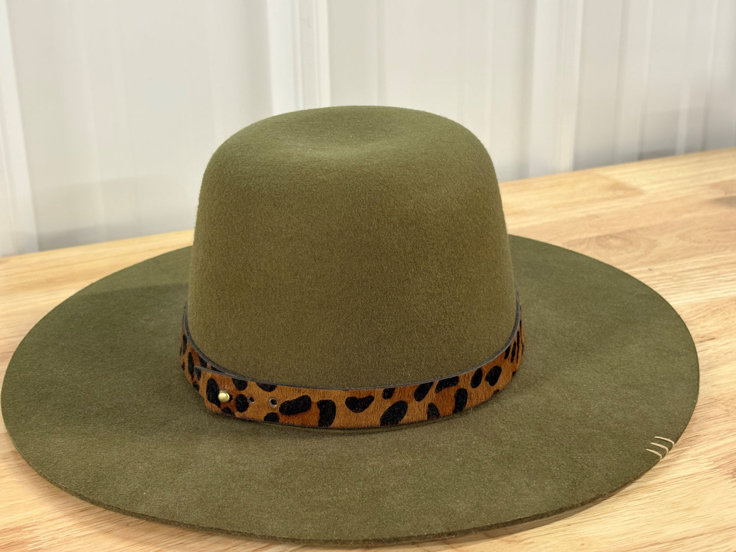 Olive green wide brim felt hat with leopard print band on a wooden table