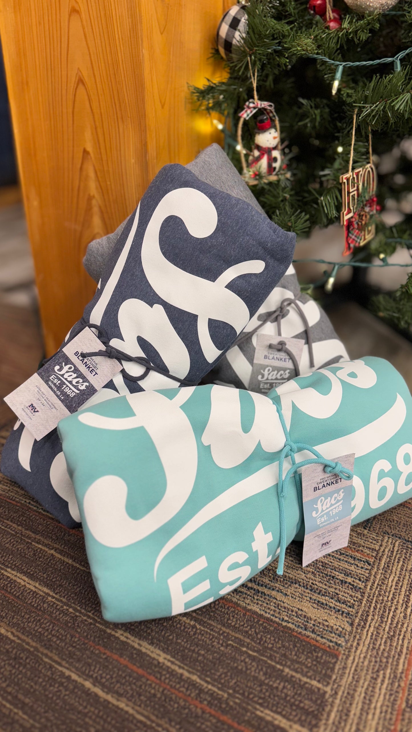 Folded branded blankets with labels, displayed near a decorated Christmas tree.