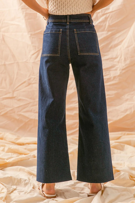 Woman wearing high-waisted wide leg dark blue jeans, back view, neutral backdrop