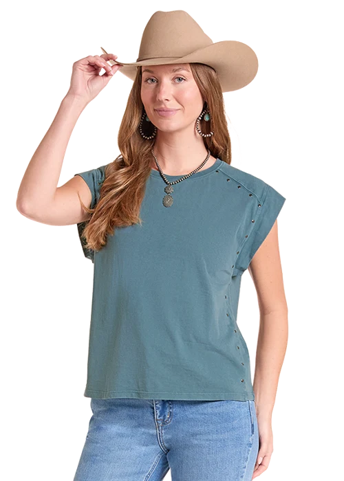 A woman wearing a muted teal short-sleeve top with decorative side studs, blue jeans, and a tan cowboy hat, posed against a plain white background.