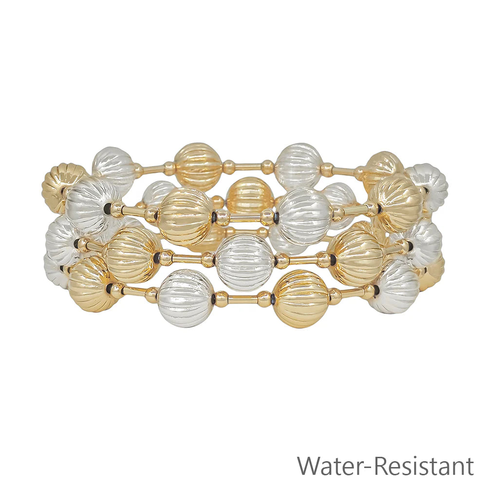 Stacked gold and silver beaded water-resistant bracelets with ribbed texture