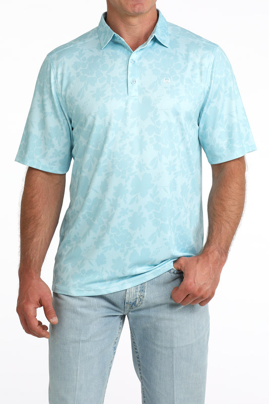 Man wearing a light blue patterned polo shirt and light blue jeans on a white background