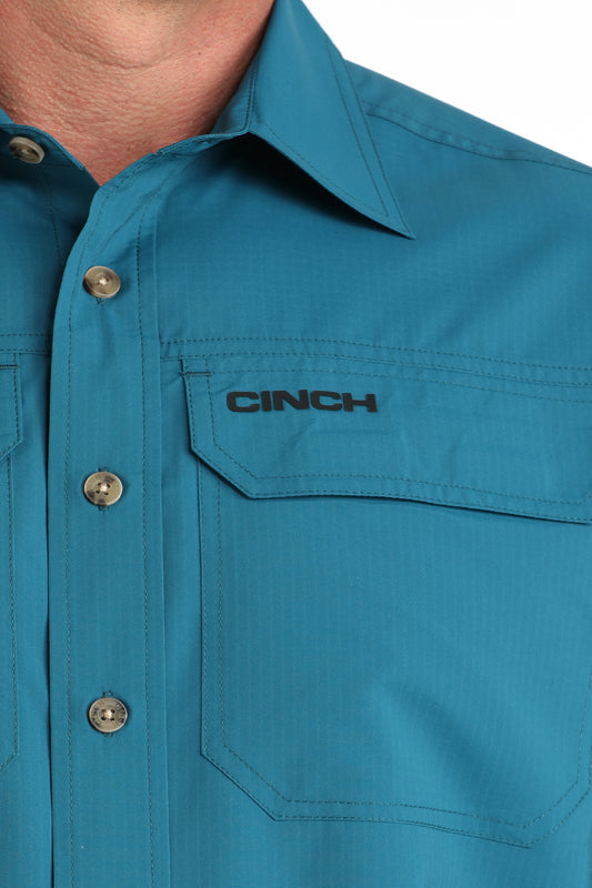 Close-up of a teal shirt with 'Cinch' logo on a white background