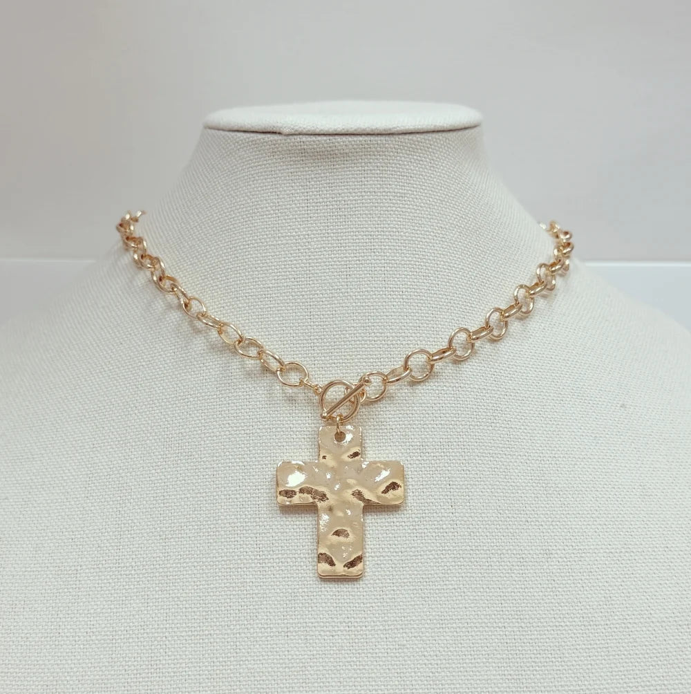 A gold-toned chain necklace with a textured cross pendant, displayed on a white fabric neck mannequin against a light gray background.