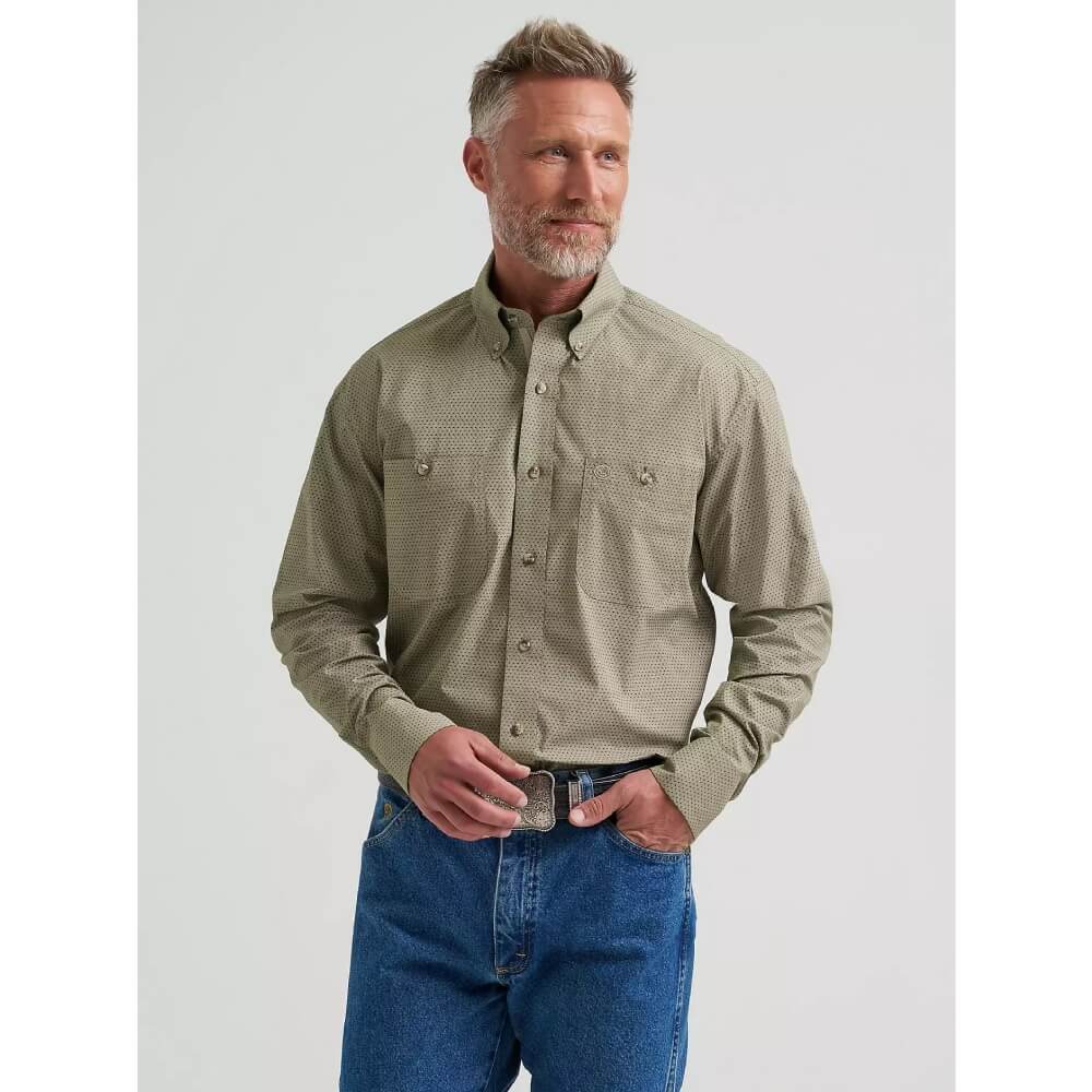 A man wearing a light olive green long-sleeve button-down shirt with a subtle textured pattern, paired with blue jeans, standing against a light gray studio background.