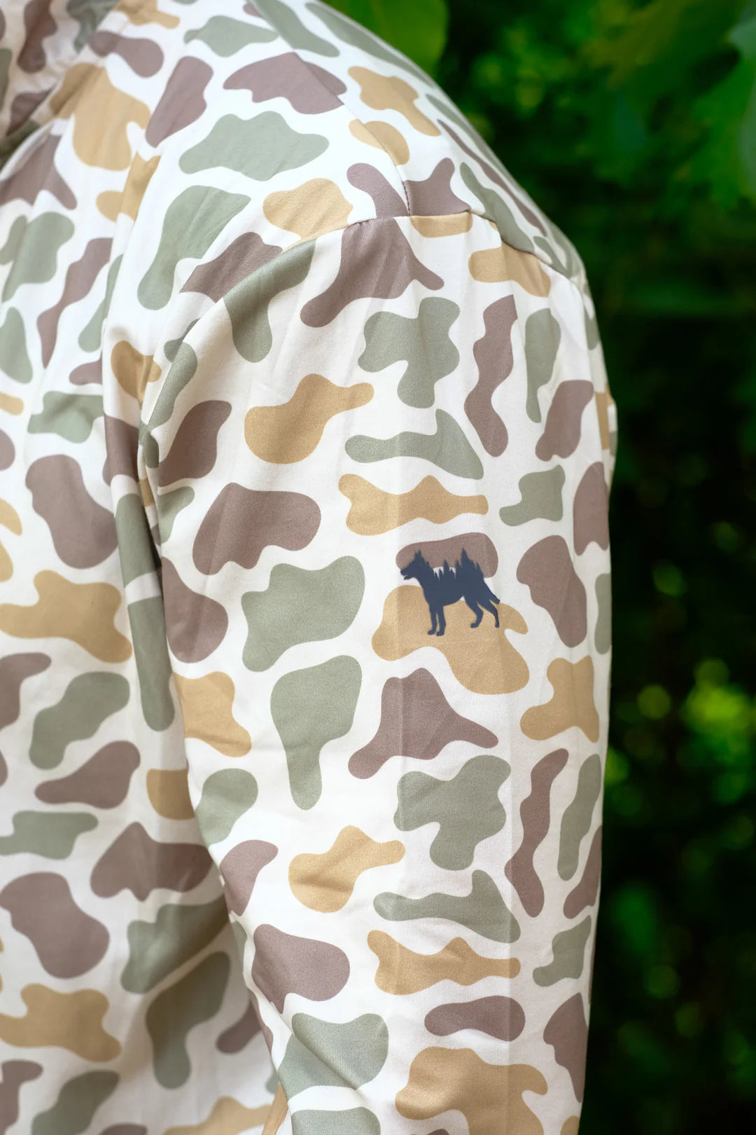 Camouflage-patterned shirt with a logo on a blurred green background