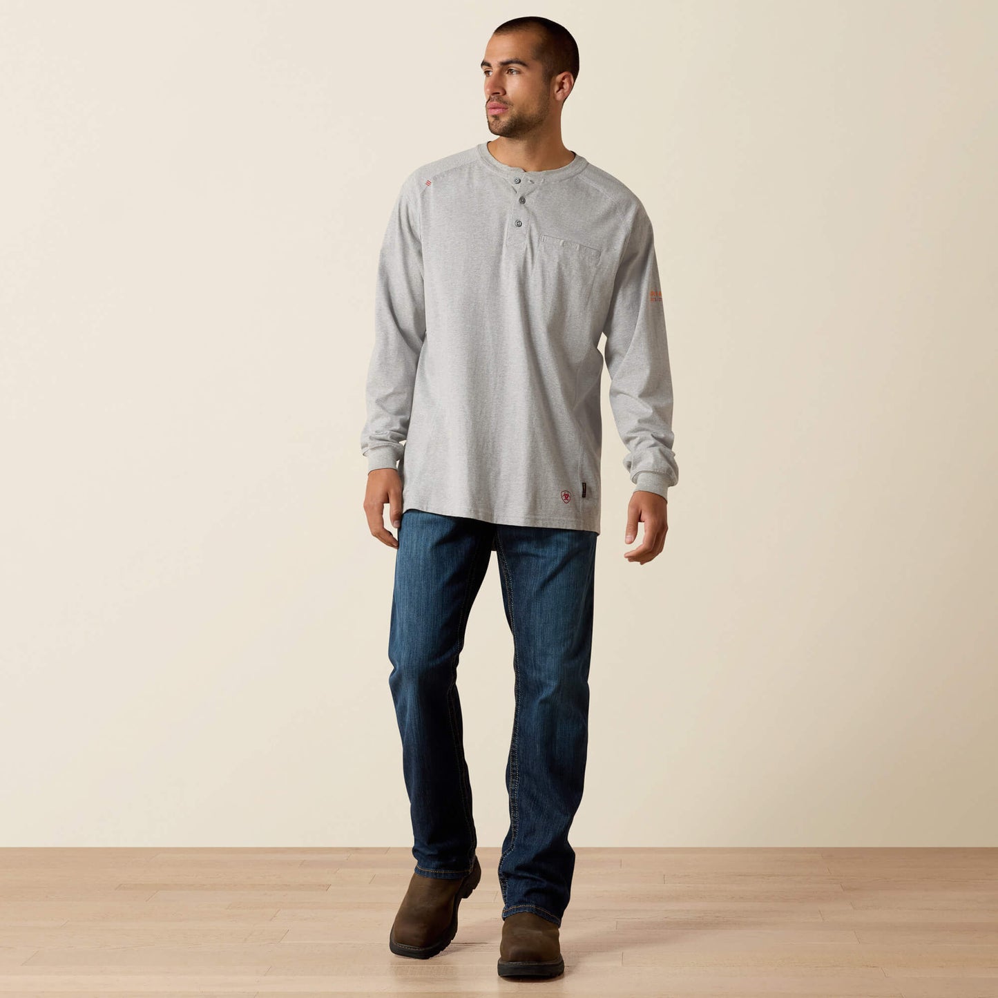 Man wearing a light gray long-sleeve shirt and blue jeans standing against a plain background