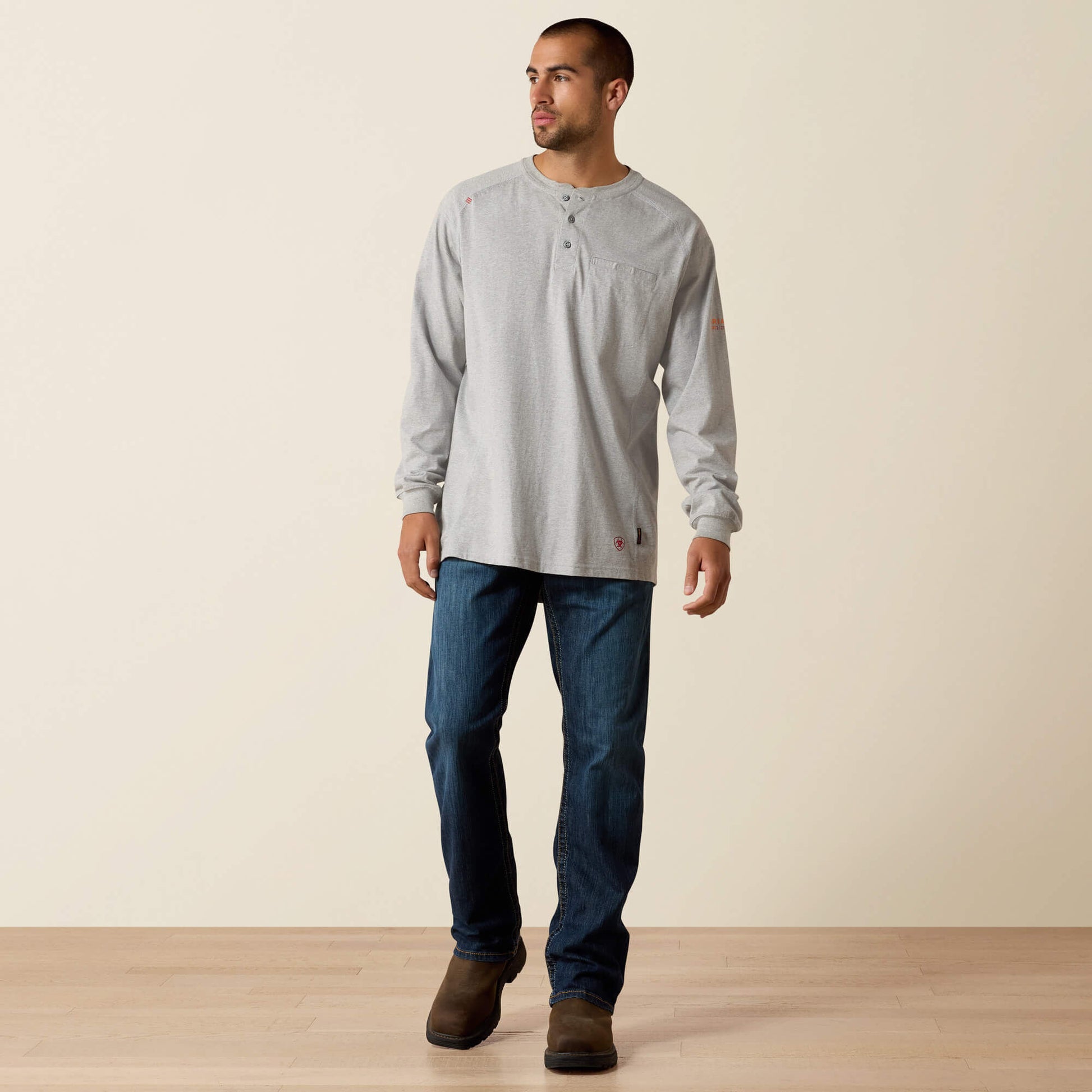 Man wearing a light gray long-sleeve shirt and blue jeans standing against a plain background