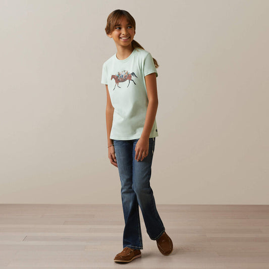 Young girl wearing a light green t-shirt with a graphic design and blue jeans, standing against a plain background.