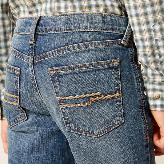 Close-up of blue jeans with a plaid shirt worn by a person.