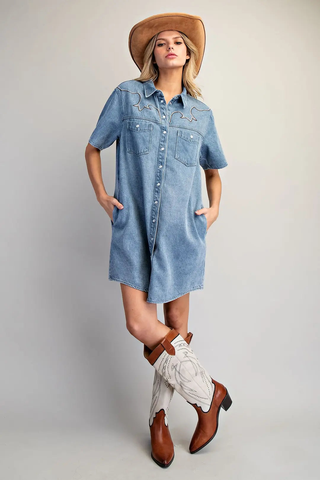 Woman wearing a denim dress, cowboy boots, and a hat on a plain background