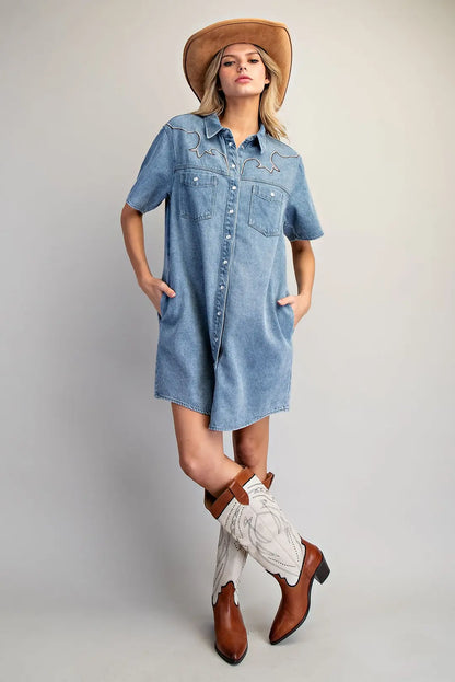 Woman wearing a denim dress, cowboy boots, and a hat on a plain background