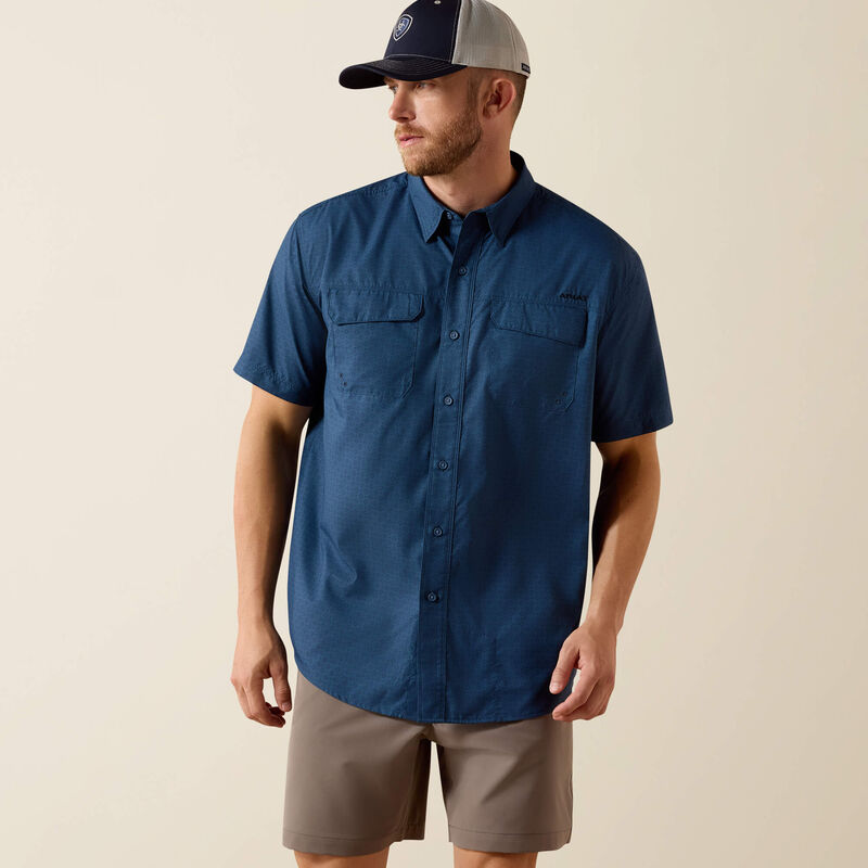 Man wearing a blue short-sleeve shirt, beige shorts, and a cap on a beige background