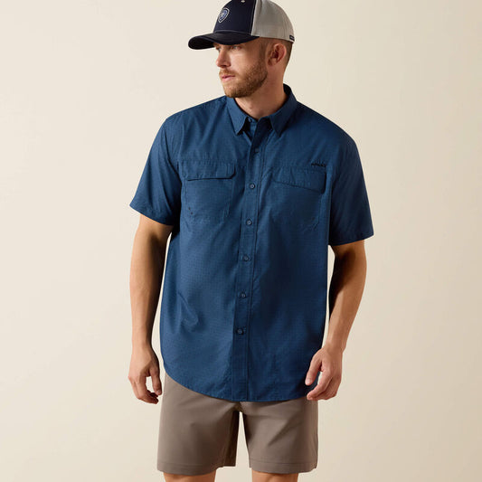 Man wearing a blue short-sleeve shirt, beige shorts, and a cap on a beige background