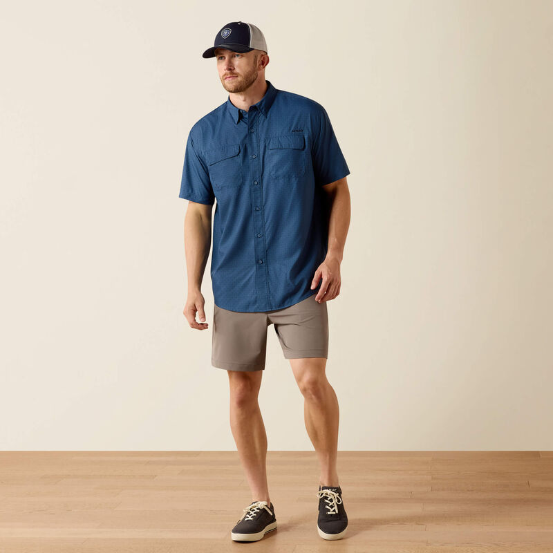 Man wearing a blue shirt, beige shorts, and a cap on a plain background