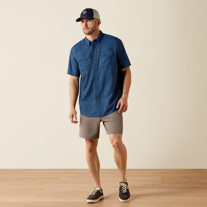 Man wearing a blue shirt, beige shorts, and a cap on a plain background