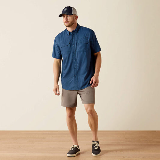 Man wearing a blue shirt, beige shorts, and a cap on a plain background