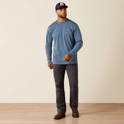 Man in blue long sleeve pocket t-shirt, gray pants, cap, and brown boots on wood floor
