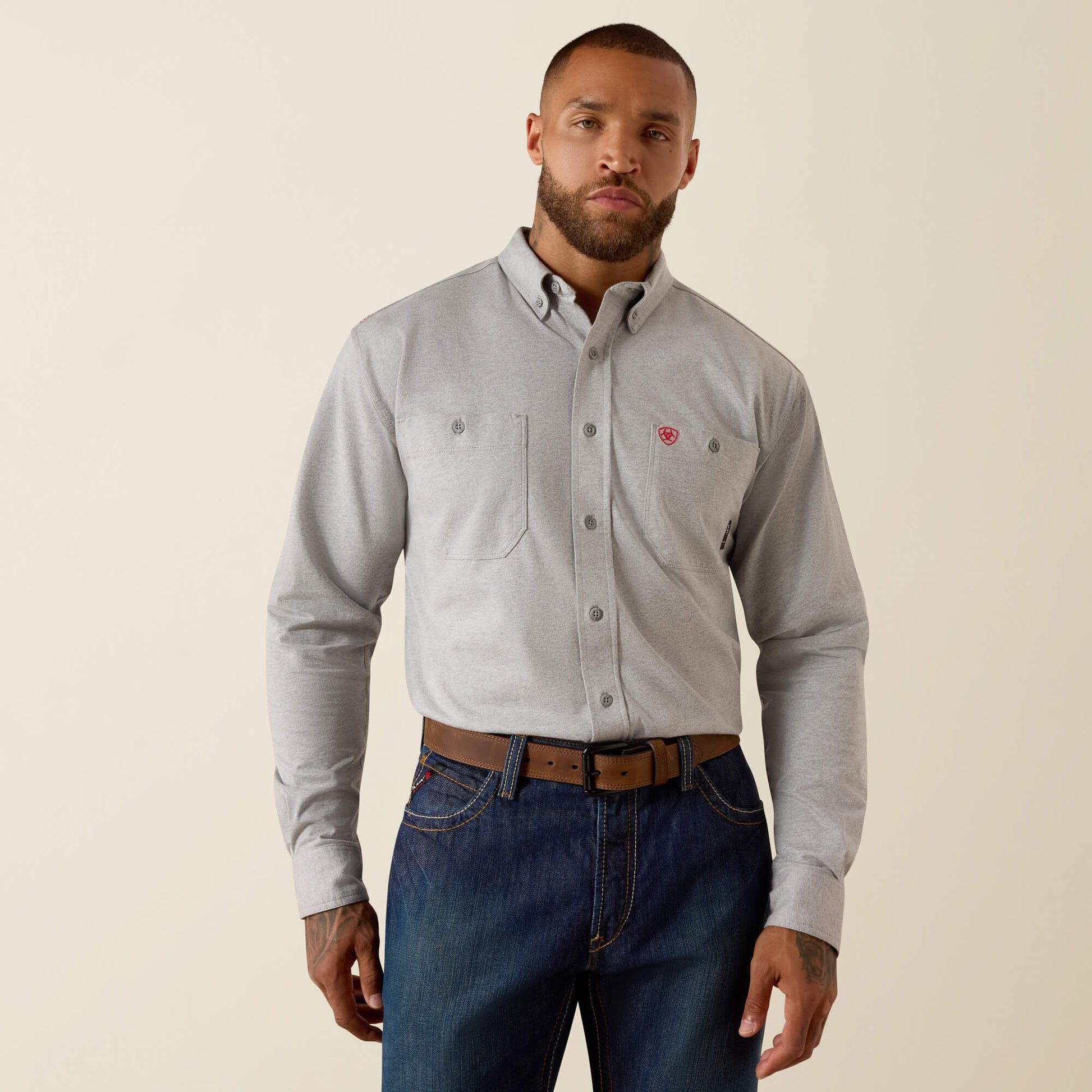 Man wearing a gray button-up shirt and blue jeans on a beige background