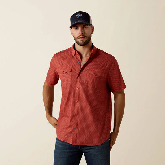 Man wearing a red short-sleeve shirt and dark cap against a beige background