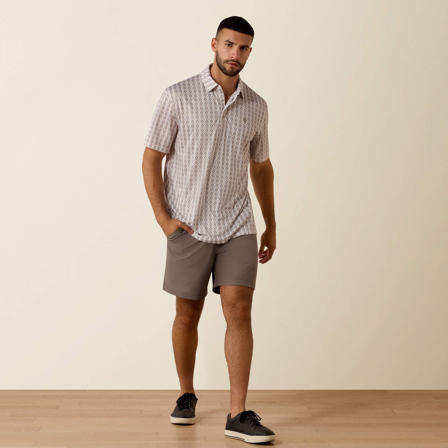 Man wearing a patterned shirt and gray shorts standing against a plain background