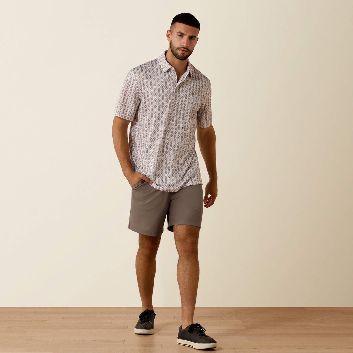 Man wearing a patterned shirt and gray shorts standing against a plain background