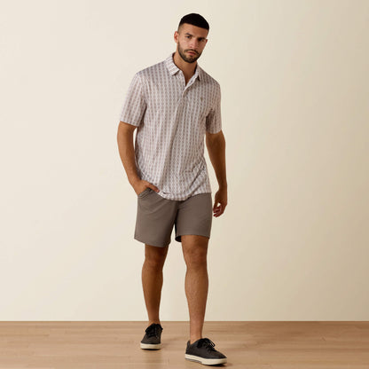 Man wearing a patterned shirt and gray shorts standing against a plain background