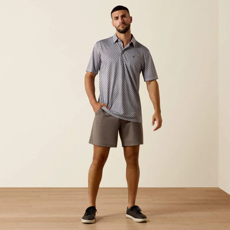 Man wearing a patterned polo shirt and shorts standing against a plain background