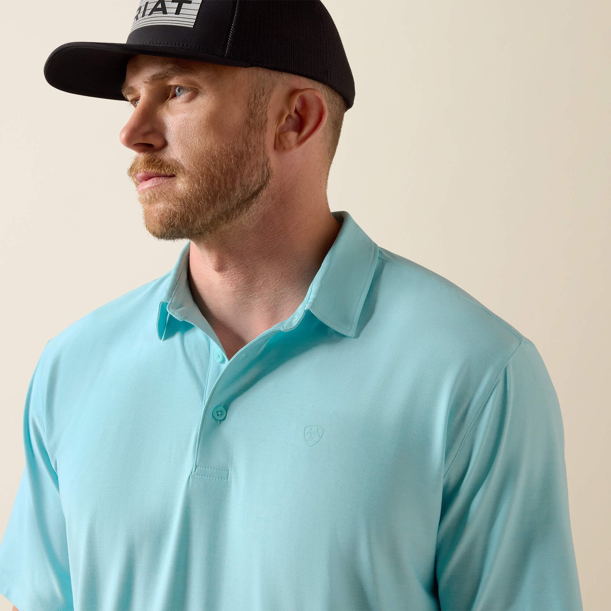 Man wearing a light blue polo shirt and black cap on a beige background