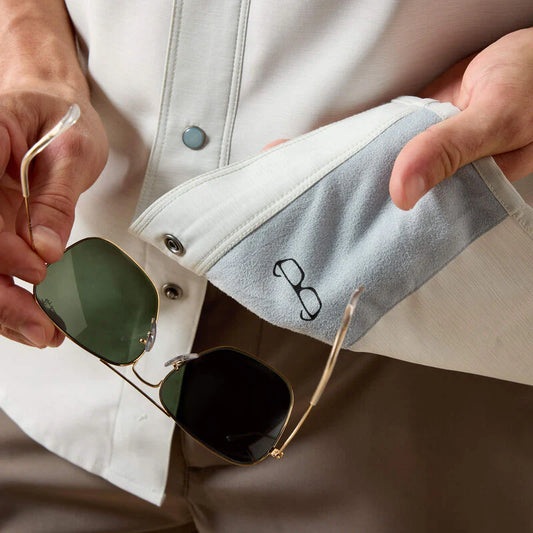 Person holding a pair of sunglasses with a white jacket and beige pants.