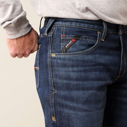 Close-up of a person wearing dark blue denim jeans, showing the back pocket with a visible Apatite brand tag and a hand pulling the waistband.