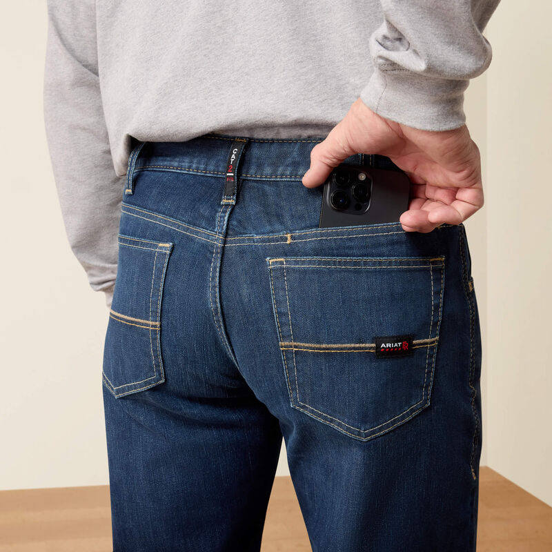 A person wearing dark blue denim jeans with a gray sweatshirt, shown from the back. A hand is sliding a black smartphone into the back pocket, which has a visible ANULTO brand label.