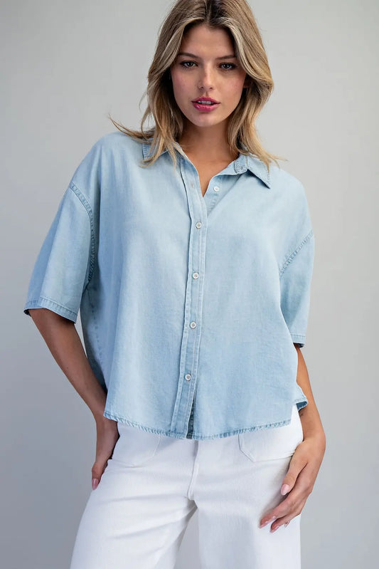 Woman wearing a light blue denim shirt and white pants on a gray background