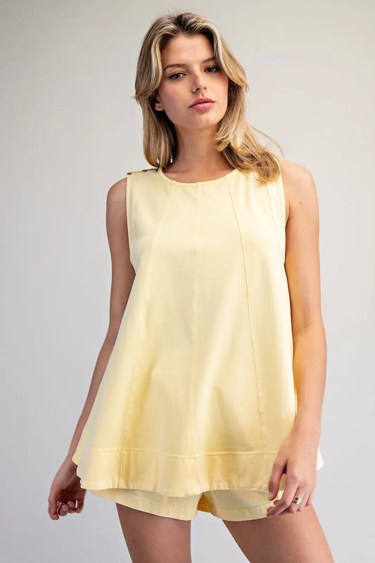 Woman wearing a light yellow sleeveless dress against a plain background